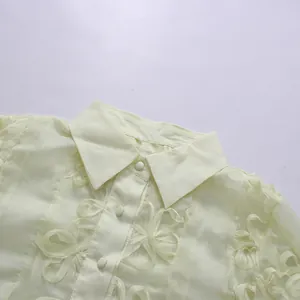 Vue macro d'une robe en mousseline jaune pâle avec détails de broderies florales en 3D.