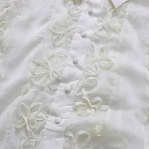Détail d'appliqués floraux 3D délicats et de boutons en tissu sur chemise en mousseline