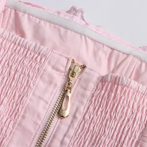 Close-up detail of a pink dress with a gold zipper and smocked fabric texture.