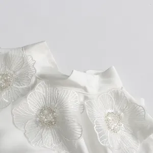 Gros plan d'une robe blanche élégante ornée de broderies florales et de perles fines