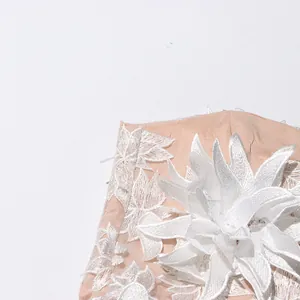 Detail view of exquisite white floral embroidery on a peach mesh dress