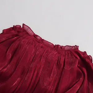 Close-up detail of a red pleated dress made from shiny mercerized fabric with ruffles