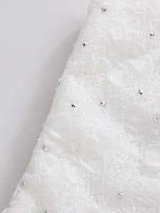 Detailed macro view of white floral lace fabric with sparkling rhinestone embellishments