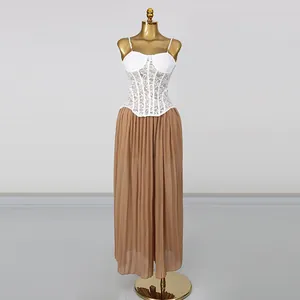 Detailansicht von weißem Spitzenkorsett-Top und braunem Falten-Maxirock-Set am Goldmannequin