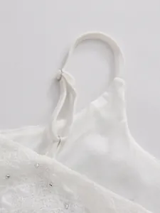 Close-up of white lace dress with adjustable strap and delicate rhinestone detailing.