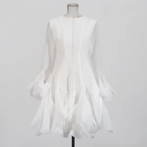 Detailweergave van de witte gelaagde jurk met ruches en uitlopende mouwen met knopen.