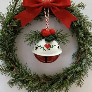 Detail eines weiß-roten Weihnachtsglocken-Ornaments, das in einem grünen Festkranz hängt