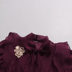 Close-up of burgundy chiffon dress with pussy-bow neck and gold flower metal ornament