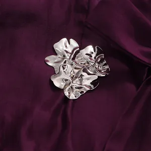 Detailed macro view of a polished silver metallic floral ornament on deep purple silk fabric