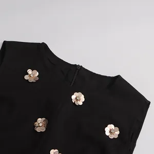 Detailed view of elegant gold metallic flower accents on a vintage black sleeveless dress.