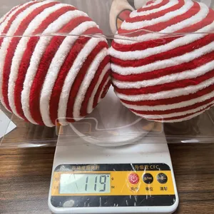Detail view of two red and white striped plush Christmas balls being weighed on a digital scale