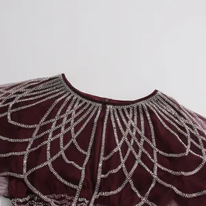Detalle de vestido burdeos con capa de malla bordada con intrincadas cuentas plateadas.