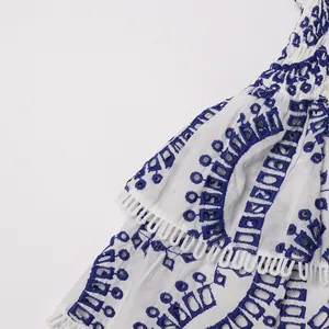 Close-up detail of blue geometric embroidery on a white Bohemian ruffle lace dress