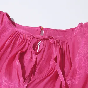 Close-up detail of the elegant bow-tie neckline on a vibrant fuchsia pleated summer dress.