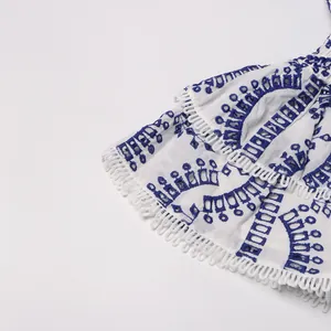 Detailed close-up of white bohemian dress featuring blue eyelet embroidery and ruffles