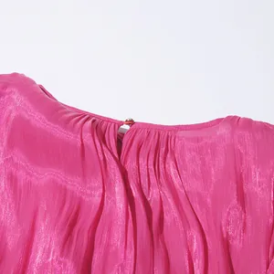 Detailed close-up of the fuchsia shimmering pleated fabric and elegant neckline button.