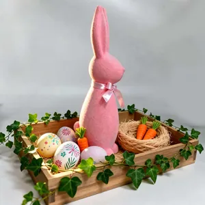 Detailed view of a pink flocked Easter bunny on a tray with festive eggs and greenery.