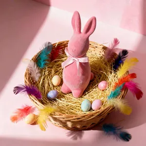 Pink flocked Easter bunny figurine with bow in straw basket with colorful feathers