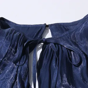 Macro detail showing the elegant tie-neck and pleated texture of the navy blue dress.