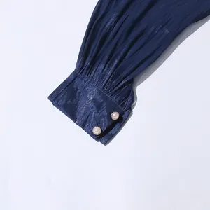 Close-up detail view of navy blue pleated dress sleeve featuring elegant pearl buttons
