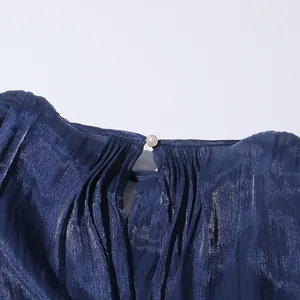 Close-up detail of the pleated neckline and pearl button on a shimmery navy blue dress