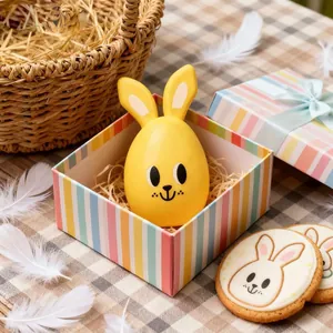 Cute yellow Easter rabbit egg toy inside a colorful striped gift box on a tablecloth