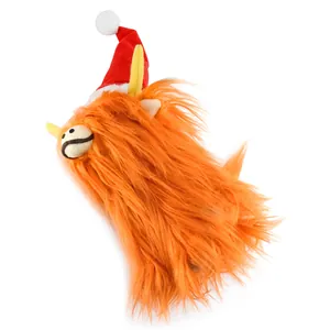 Primer plano de un adorno de peluche de vaca Highland naranja con gorro de Navidad rojo.