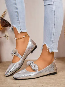 Elegant silver textured Mary Jane flat shoes with bow detail worn with denim jeans