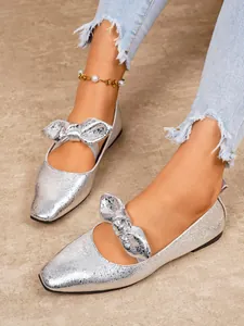 Close-up detail of shiny silver Mary Jane flats with bow decoration