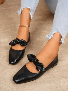 Close-up of chic black Mary Jane flats featuring a large bow and glossy finish.