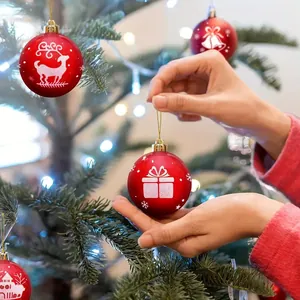 Hand hanging a red Christmas ornament ball with a gift print on a decorated tree