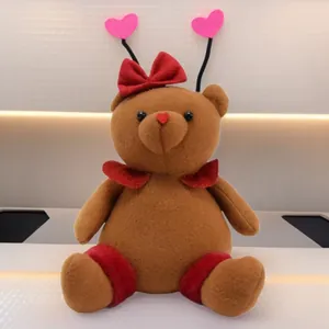 Detailed close-up view of a cute brown teddy bear plush with a red bow and pink heart antennas