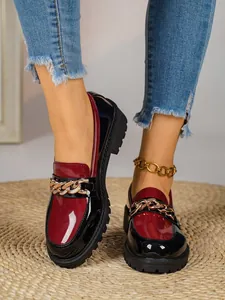 Κοντινό πλάνο από κομψά μπορντό λουστρίνι loafers με πλατφόρμα και χρυσή αλυσίδα.