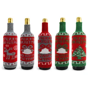 Five knitted Christmas wine bottle covers with reindeer, tree, and bow designs.