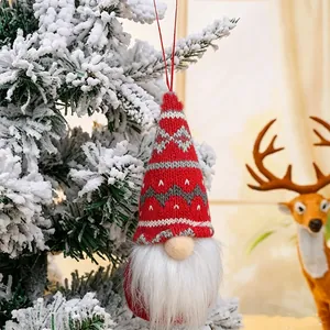 Detail of a red knitted Nordic gnome ornament hanging on a snowy Christmas tree