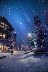 Enchanting snowy village landscape at night with glowing Christmas lights and falling snow