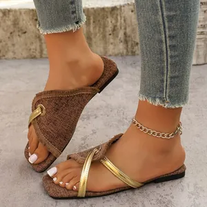 Nahaufnahme von stilvollen braunen flachen Web-Sandalen mit goldenen Riemen für Damen am Fuß