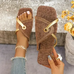 Nahaufnahme flacher Damen-Sandalen aus braunem Stoff mit metallischen goldenen Riemen.
