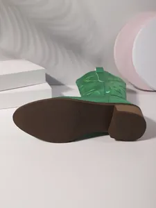 Detailed view of the anti-slip brown sole and block heel of a green cowboy boot.