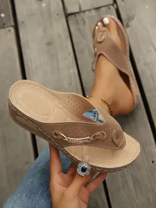 Primer plano de chanclas de cuña marrones con detalle de cadena dorada en madera