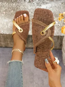 Nahaufnahme braune flache Sandale mit goldenen Riemen und metallischem Ringdetail
