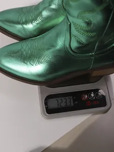 Close-up showing a metallic green western style boot weighing 723.3g on a digital scale