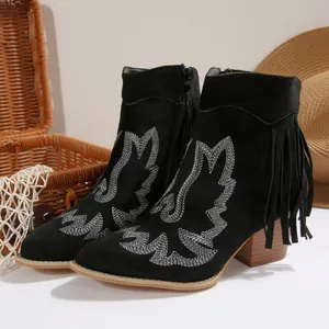 Detailed view of black suede western boots with white embroidery and side fringe