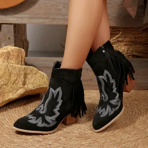 Close-up detail of black western ankle boots featuring white embroidery and side fringes.