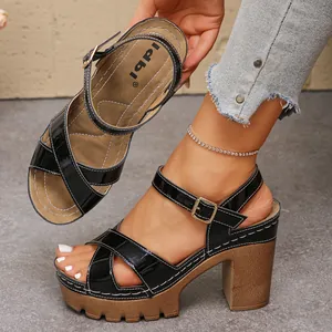 Detail view of black patent leather platform sandals with chunky wood-grain heels and cross straps.