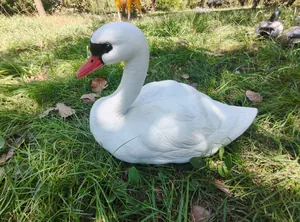 Side view of realistic white swan garden statue placed on grass in a natural garden