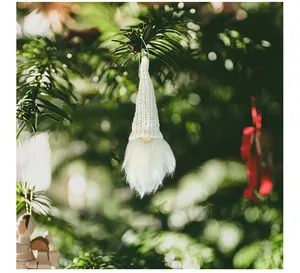 Close-up of a white knitted gnome ornament with sequins hanging on a Christmas tree