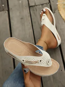 Primer plano de chanclas de cuña blancas con cadena dorada y detalles cortados por láser