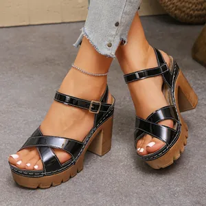 Close-up view of black patent leather platform sandals with cross-straps worn on feet