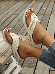 Primer plano de sandalias de cuña blancas para mujer con cadena dorada en los pies